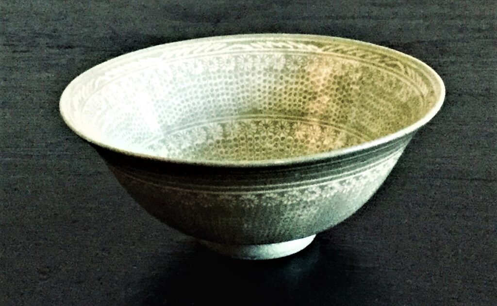 淡い青緑色の釉薬がかかった龍泉窯風の茶碗。繊細な文様が施されている。